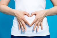 person holding hands in heart shape over stomach